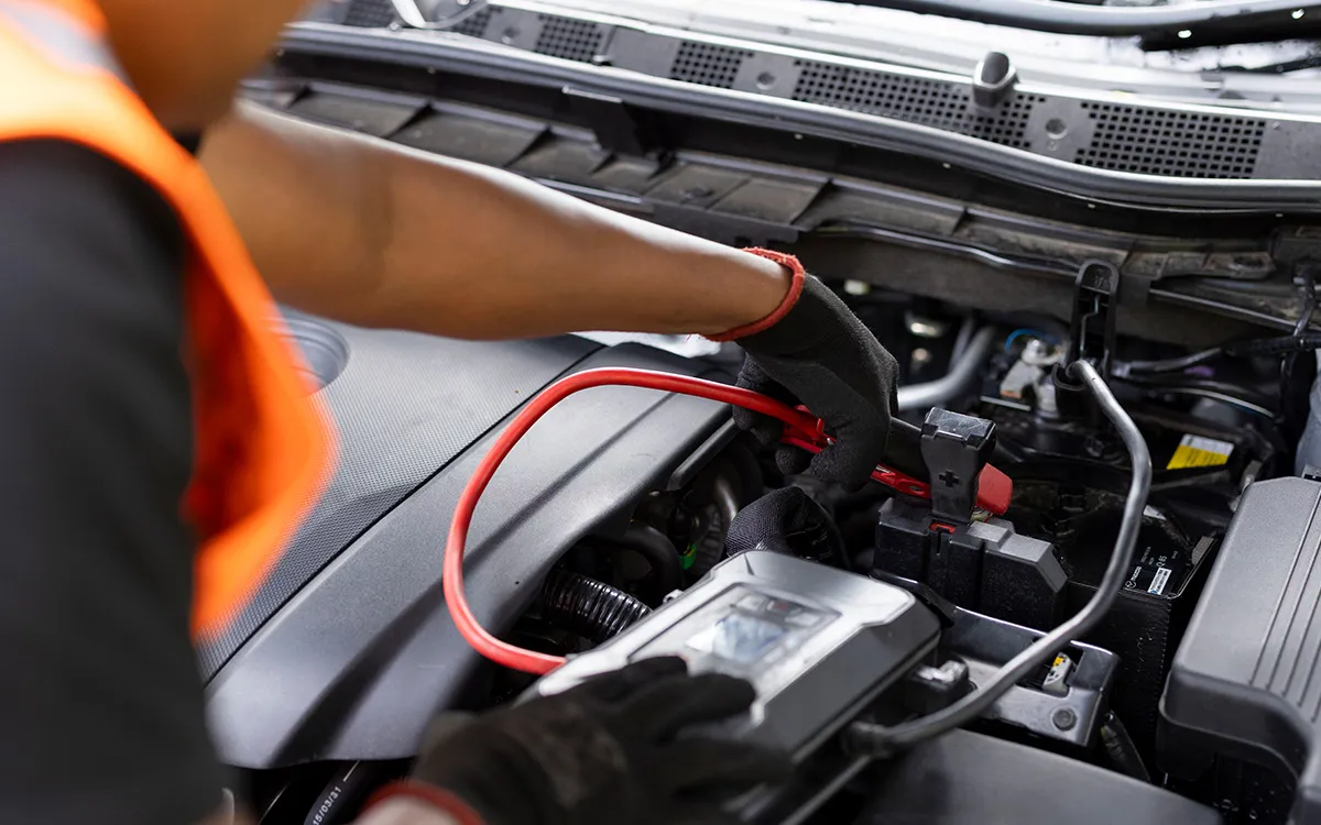 AMI MotorHub technician testing a car battery under the bonnet.