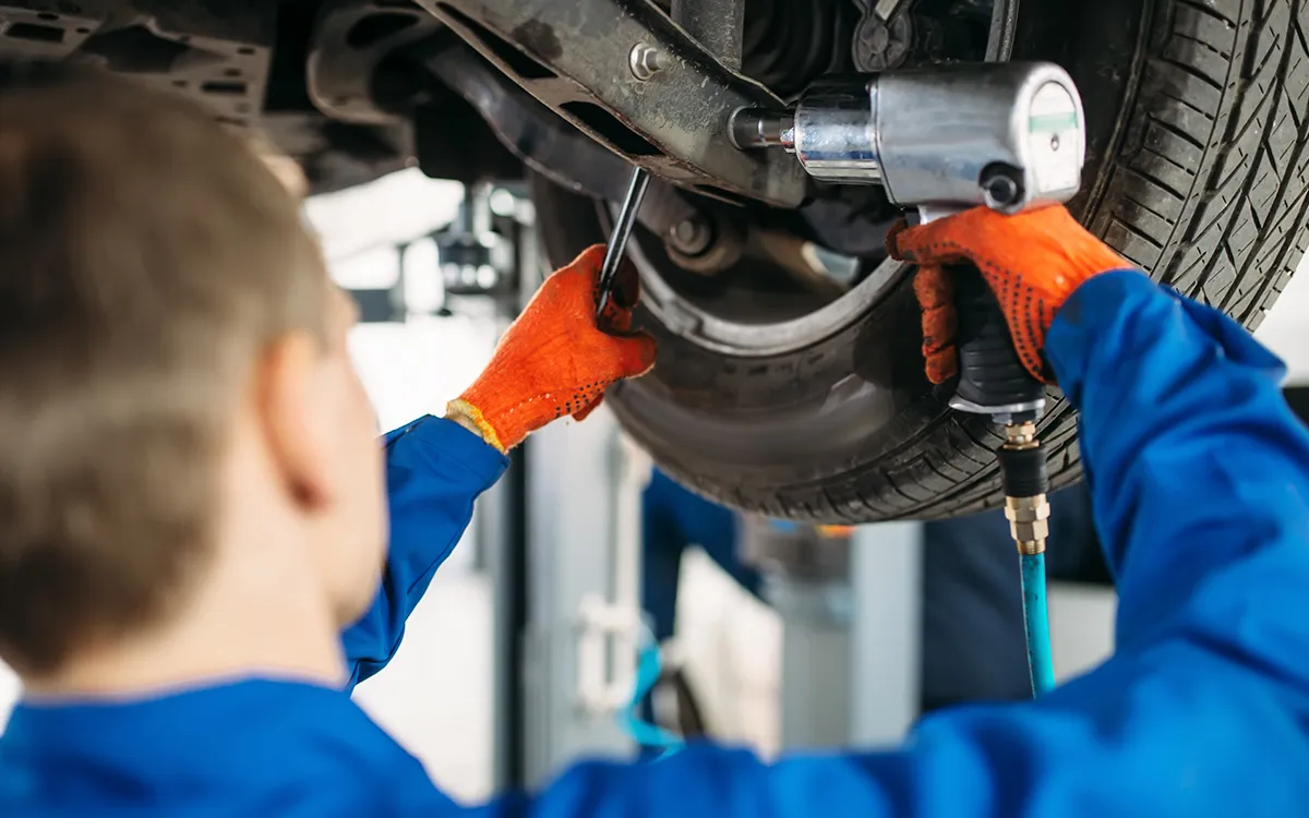 AMI MotorHub technician working on a vehicle's suspension and steering components on a hoist.